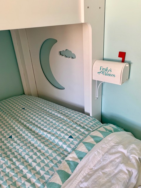 photo of a child's bedroom with a mailbox affixed to the bed. The mailbox says "Emily's glasses"
